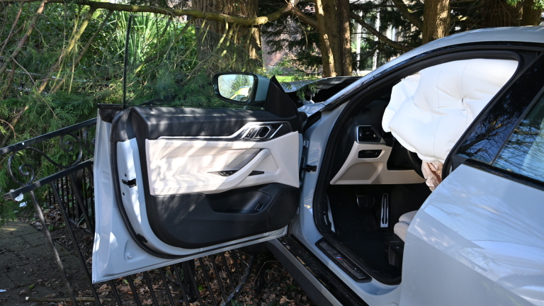 Een zilveren auto is tegen een boom gereden met de airbags uitgeklapt; enkele mensen staan er omheen te kijken.