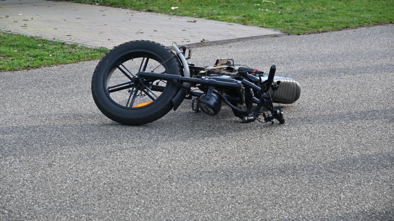 Een ambulance staat geparkeerd naast een rode auto op een straat, terwijl twee mensen zich buigen over spullen op de grond.