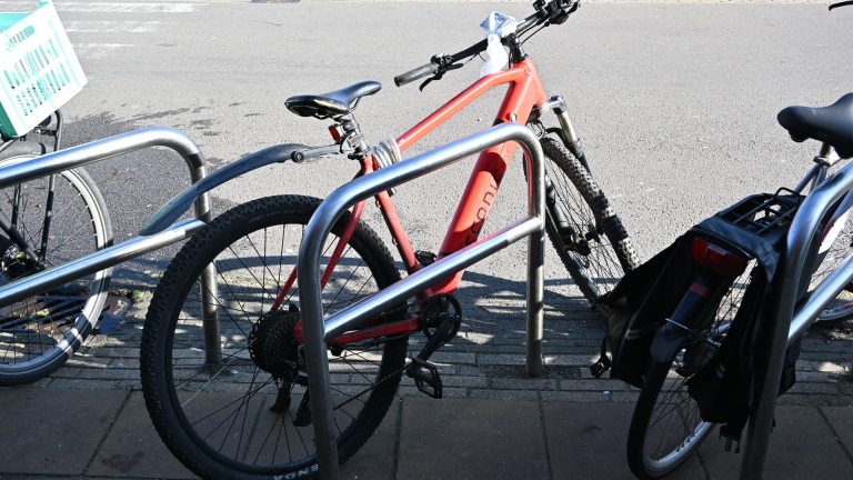 Een politieauto en een ambulance staan geparkeerd voor een gebouw met glazen gevel, omringd door enkele mensen en fietsen.