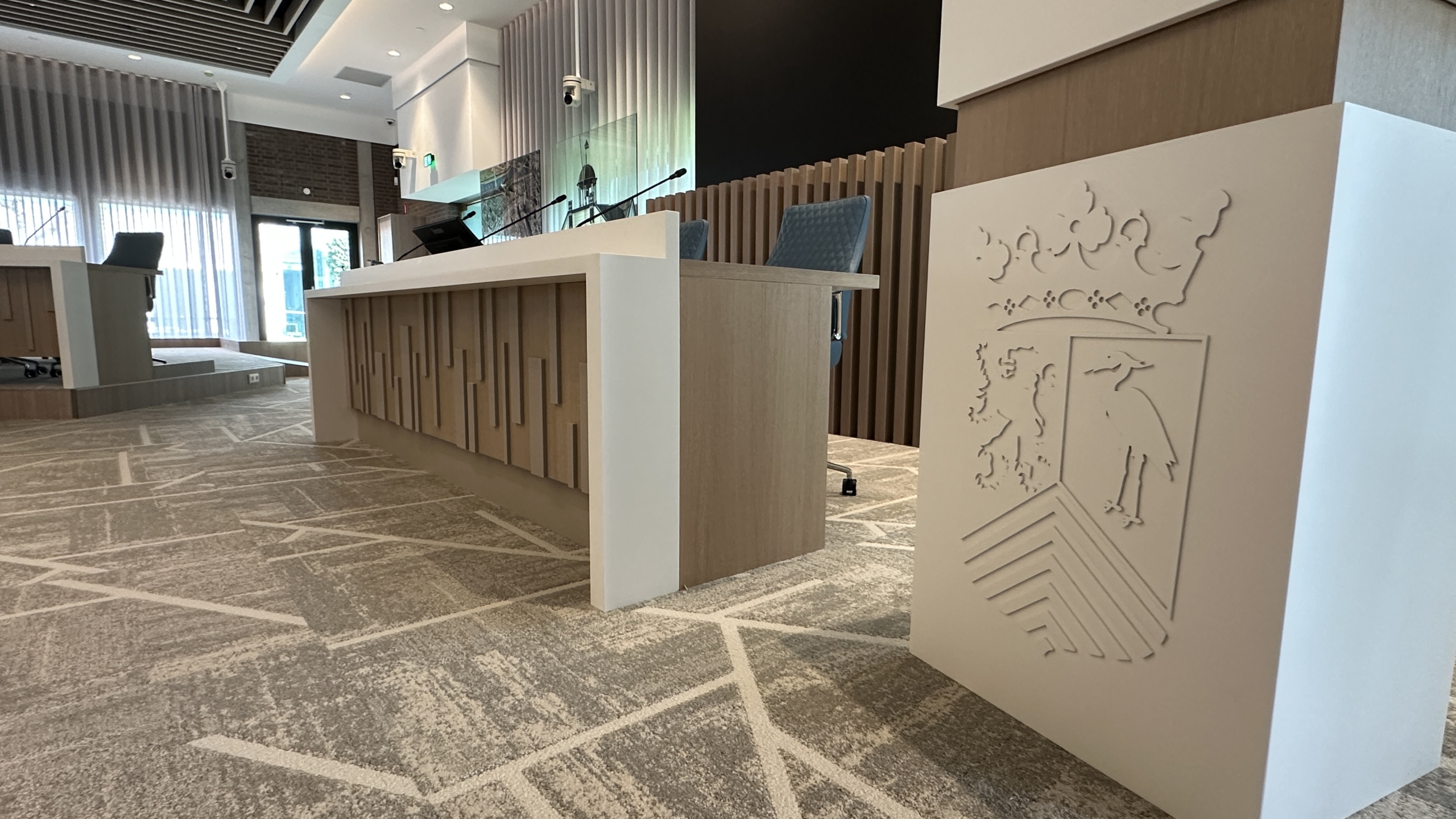 Vergaderzaal met rondom een grote ovale tafel, blauwe stoelen en moderne hanglampen aan het plafond.