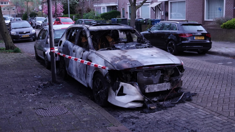 Uitgebrande auto met geblakerd exterieur en politieafzetlint, geparkeerd op een straat.