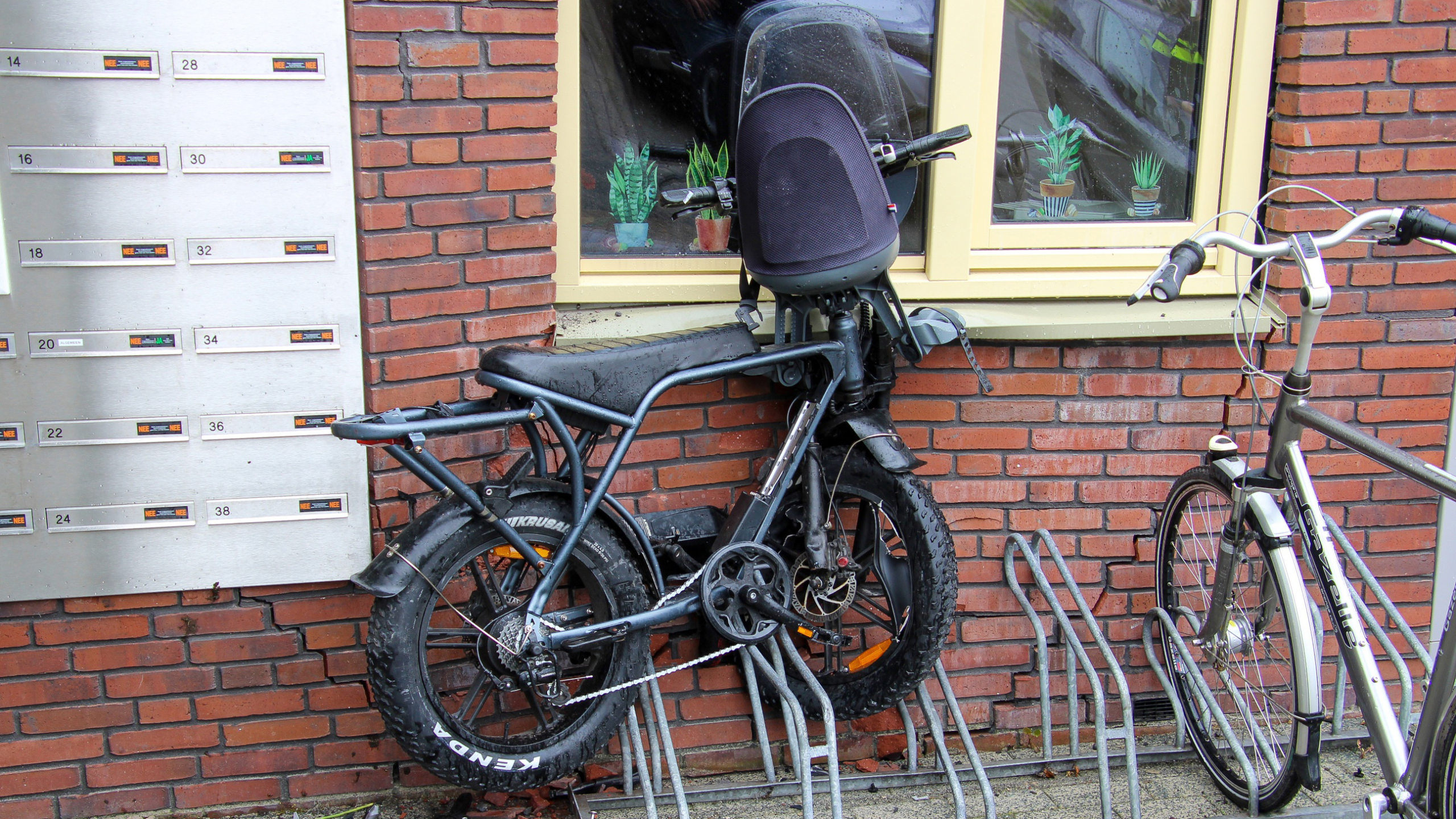 Fietsen geparkeerd naast een bakstenen muur met brievenbussen en een venster.