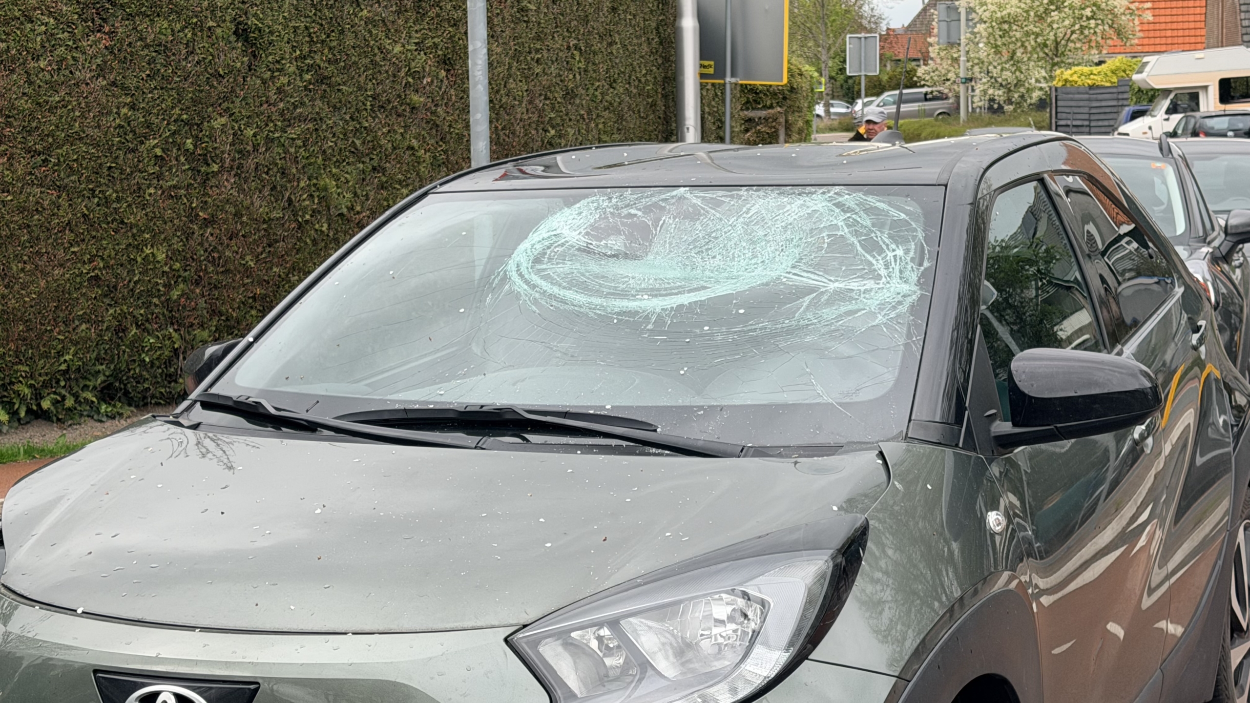 Politieagenten en een ambulance op een kruispunt, met enkele mensen bij een auto betrokken bij een incident.