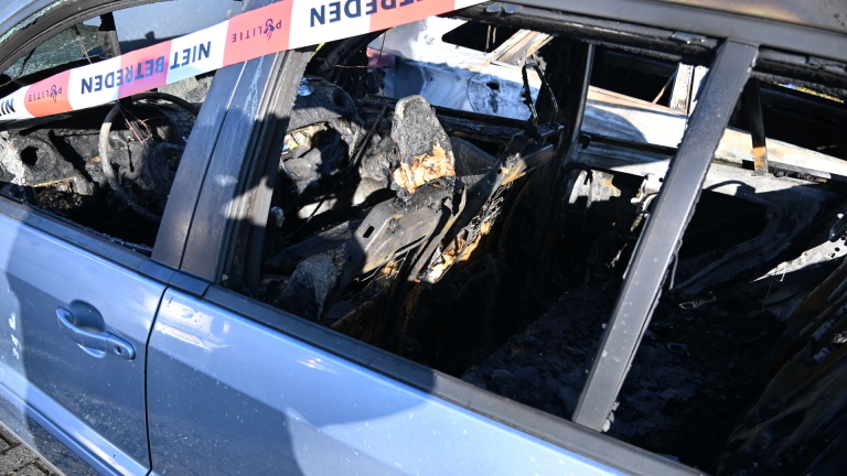 Twee uitgebrande auto's met geopende motorkappen, omgeven door afzetlint, geparkeerd in een woonwijk.