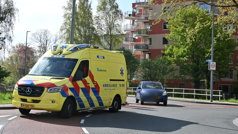 Politieagenten en ambulancepersoneel bij een ongeval; politie motorfiets op de voorgrond, met een geopende ambulance op de achtergrond.