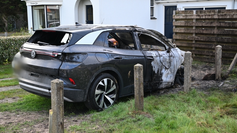 Uitgebrande auto met ernstig beschadigd motorblok en carrosserie, geparkeerd op een onverharde weg.