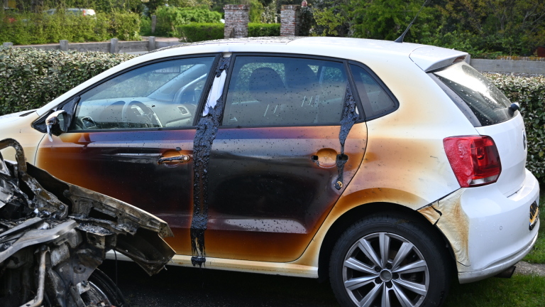 Uitgebrande auto met ernstig beschadigd motorblok en carrosserie, geparkeerd op een onverharde weg.
