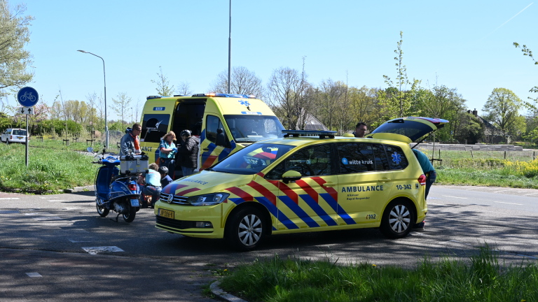 Twee ambulances staan op straat bij een verkeersongeval, met hulpverleners die zich bezighouden met een motorfiets en andere voertuigen.