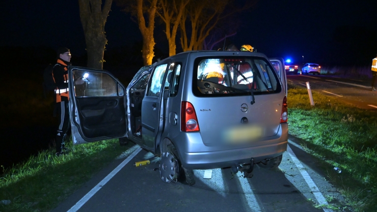Auto met schade aan een kant van de weg in het donker, met een persoon en politie in de buurt.