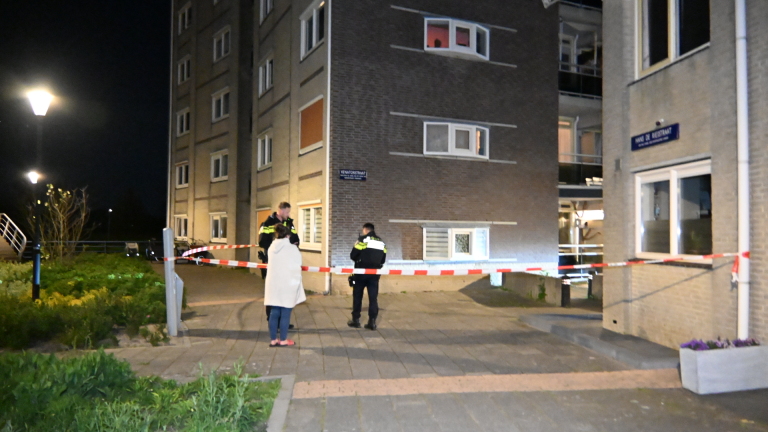 Politieagent aan de telefoon bij een kapot raam in een gebouw, gefotografeerd in het donker.