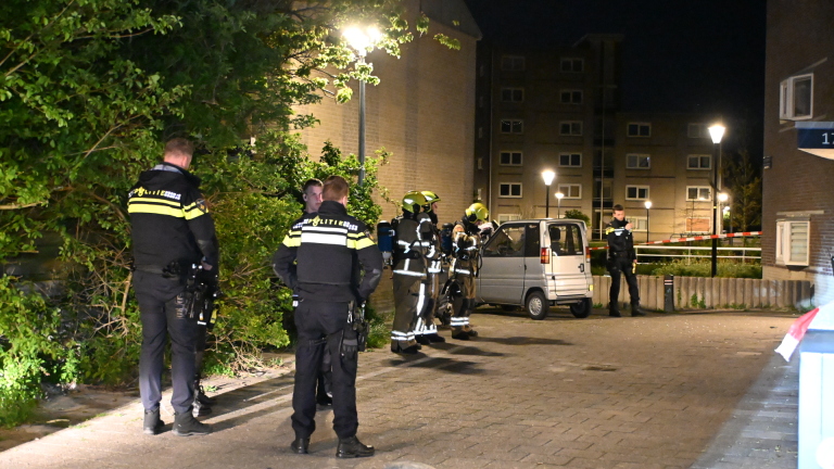 Politieagent aan de telefoon bij een kapot raam in een gebouw, gefotografeerd in het donker.