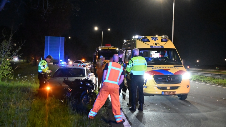 Hulpdiensten bij een ambulance op een weg in de nacht, omringd door bomen en straatverlichting.