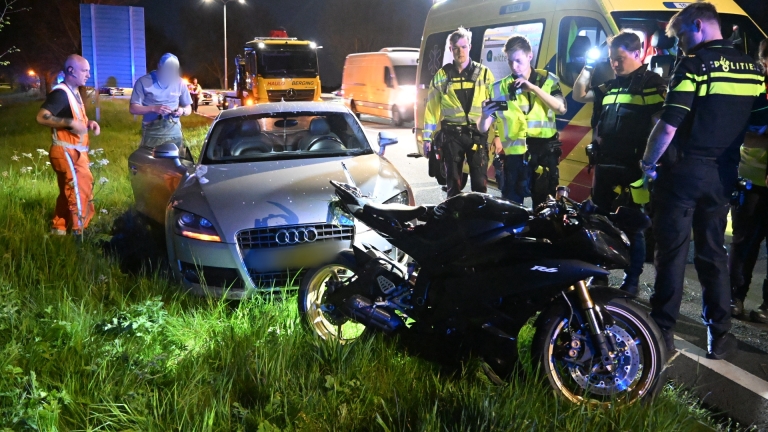 Hulpdiensten bij een ambulance op een weg in de nacht, omringd door bomen en straatverlichting.