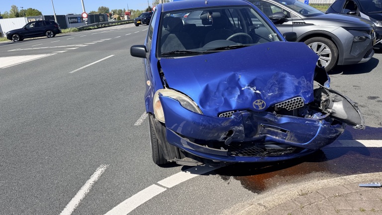 Blauwe auto met zware schade aan de voorkant op de straat, met een plas vloeistof op de grond.