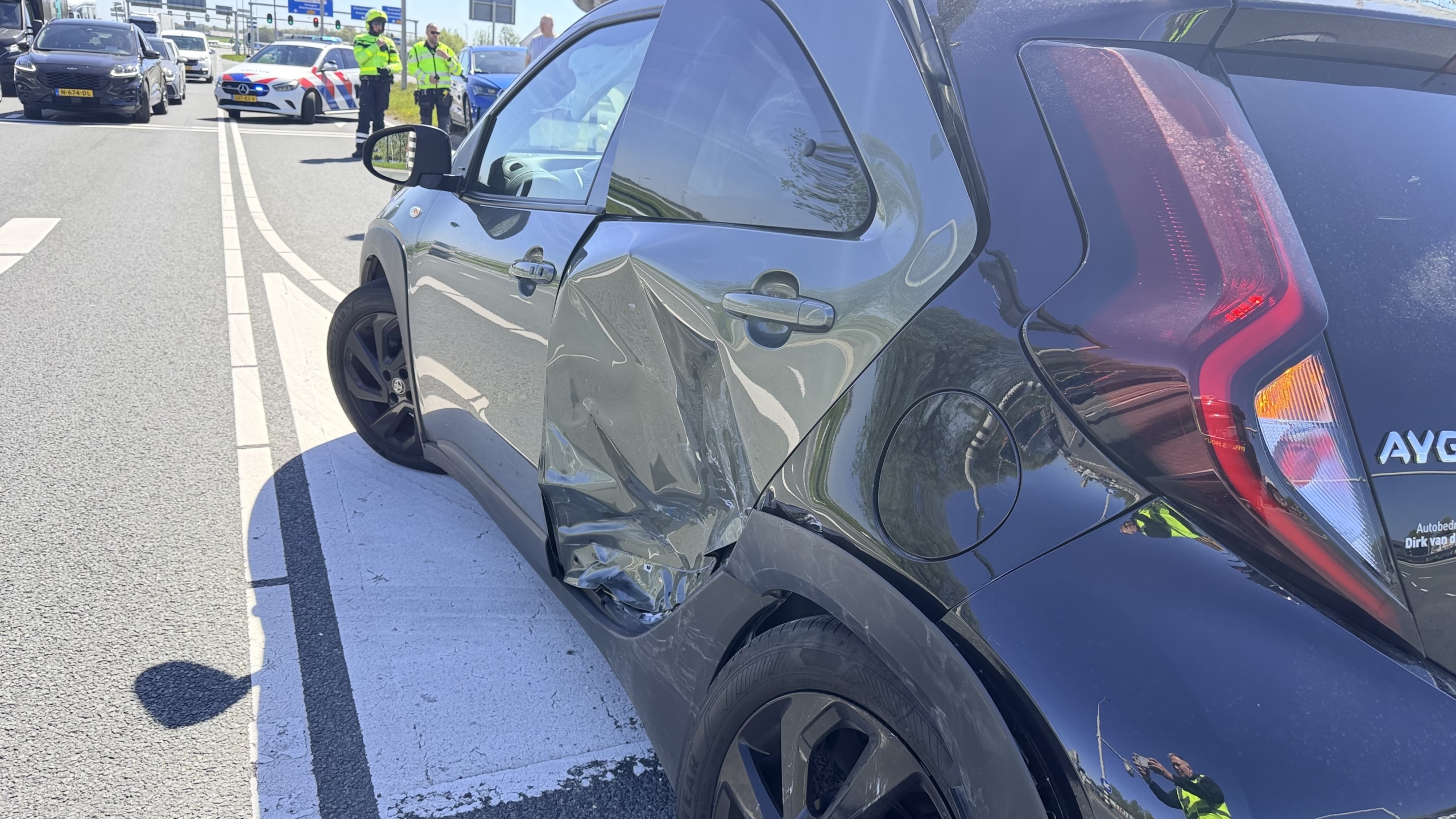 Blauwe auto met zware schade aan de voorkant op de straat, met een plas vloeistof op de grond.