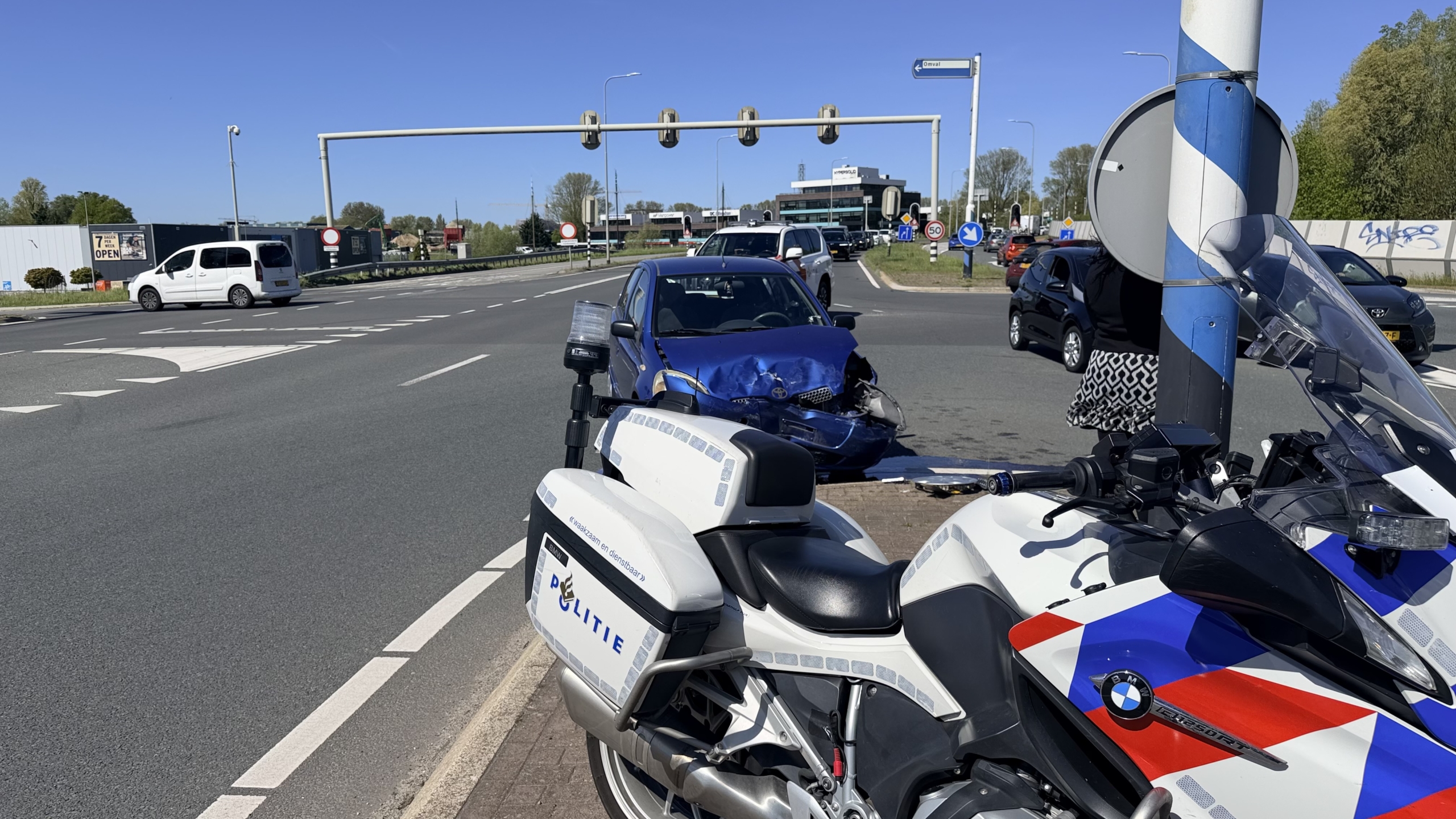 Blauwe auto met zware schade aan de voorkant op de straat, met een plas vloeistof op de grond.