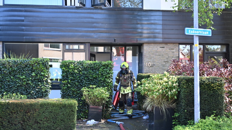 Brandweerlieden in beschermende uitrusting staan bij een brandweerwagen met uitgerolde slangen voor een modern huis.