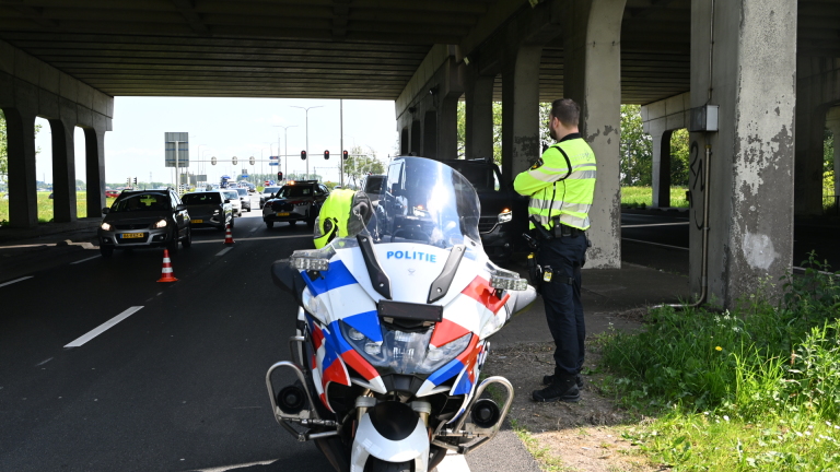 Politiecontrole onder viaduct met agenten in reflecterende kleding, een politie-motorfiets en passerende auto's.