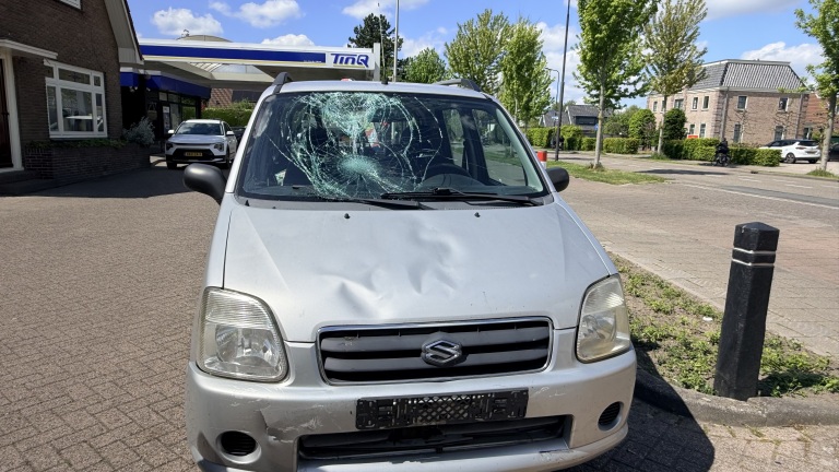 Auto met ingedeukt voorpaneel en gebarsten voorruit, geparkeerd bij een tankstation op een zonnige dag.