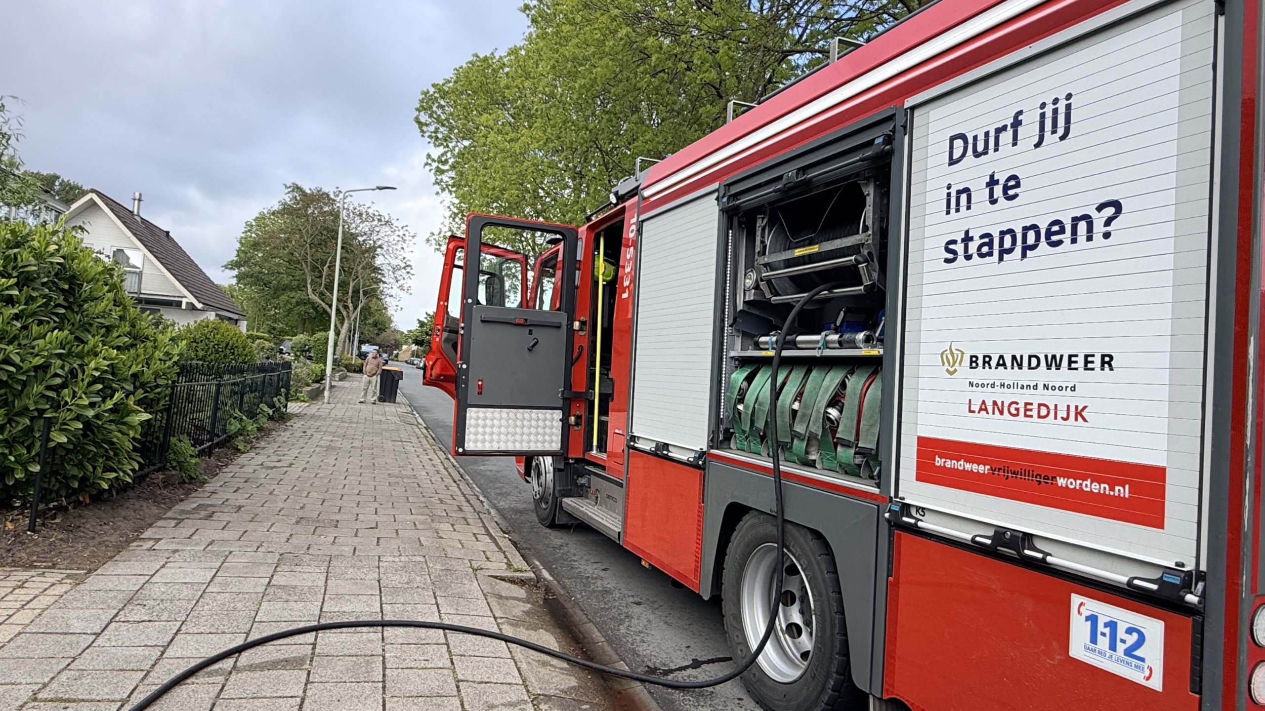 Brandweerman in beschermende kleding betreedt een gebouw met rookontwikkeling naast een woonhuis met een nummer 16.