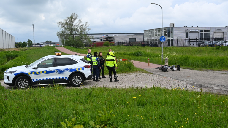 Politieagenten bespreken een incident met een omgevallen scooter op een fietspad.