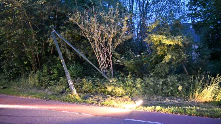 Een gekantelde auto ligt op de weg naast een politieauto met zwaailichten, omgeven door bomen bij schemering.