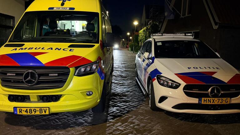 Hulpverleners bij een ambulance verzorgen iemand naast een gebouw, terwijl een scooter op de voorgrond staat.