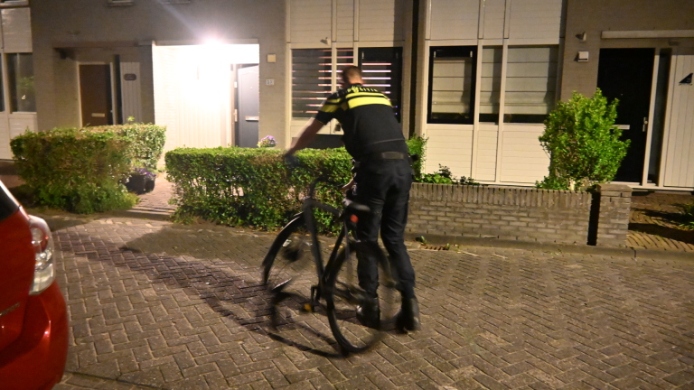 Tuin omheind met rood-wit lint bij nacht, man staat naast een huis met gesloten jaloezieën.