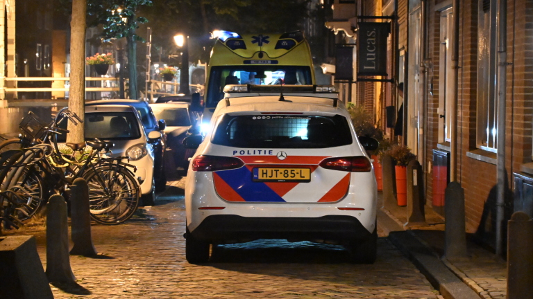 Nachtelijke scène met een ambulance en politieauto voor een gebouw, omringd door hulpverleners, met een persoon in het water.