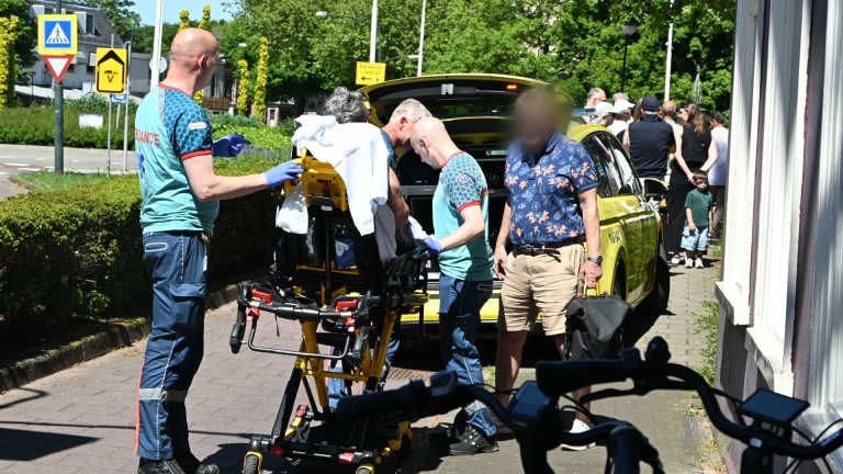 Ambulancepersoneel helpt een persoon op de stoep naast een ambulance; een jongen kijkt toe.