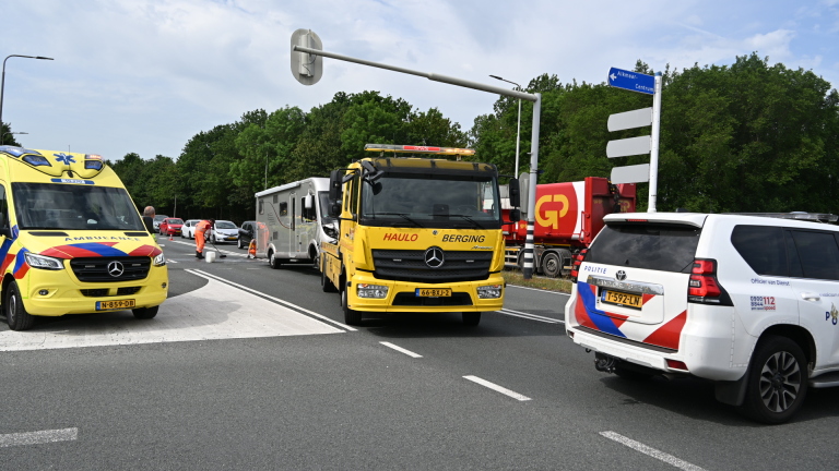 Verfrommeld voertuig betrokken bij ongeval langs de weg, met een brandweerman en een hulpverlener naast een ambulance.