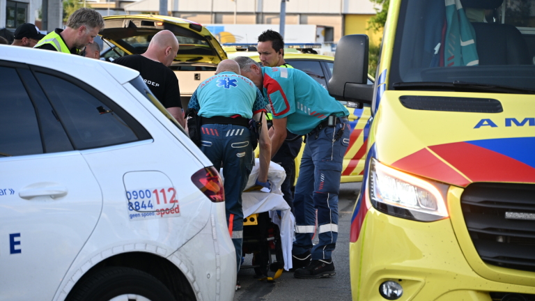 Politie- en ambulancevoertuig staan geparkeerd op straat naast mensen met een brancard, waarschijnlijk bij een noodsituatie.