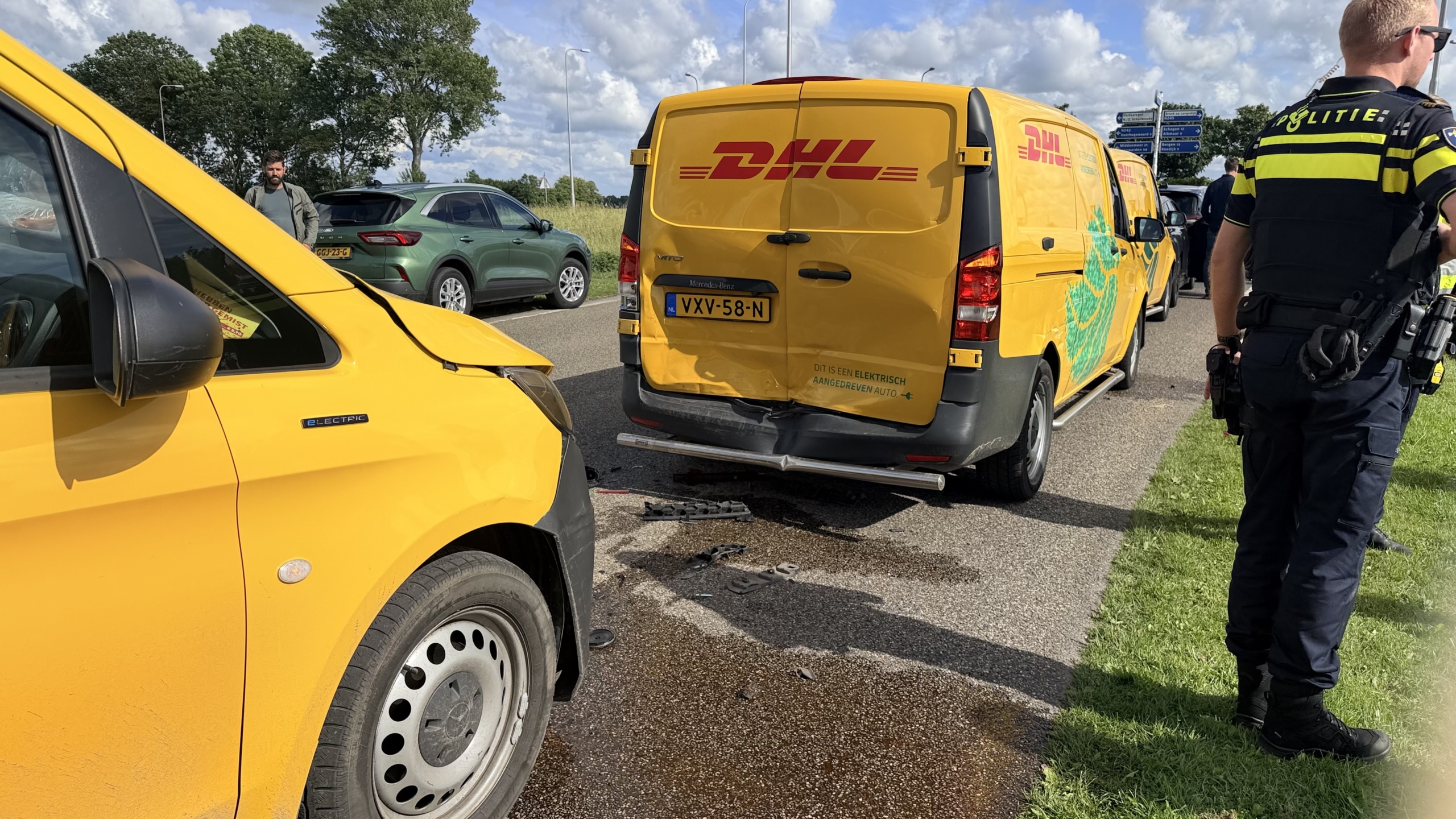 Gele DHL-bestelwagens met groene patronen staan langs de weg; politie en mensen kijken toe.