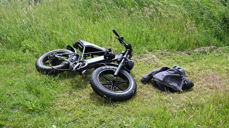 Een grijze bestelwagen staat geparkeerd naast een bouwterrein met een graafmachine, naast een ambulance en agenten.