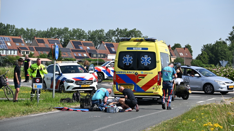 Twee mensen in sportkleding verlenen hulp aan een persoon naast een fiets, met een kijker en een verkeersbord op de achtergrond.