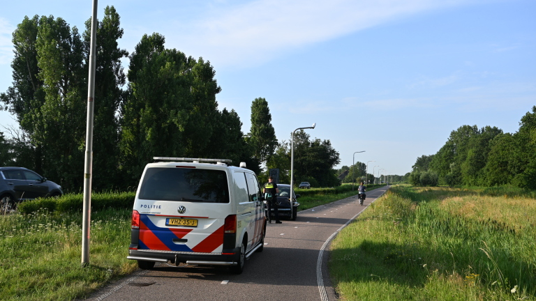 Auto gebotst tegen lantaarnpaal op rustige weg, met agent die schade inspecteert.