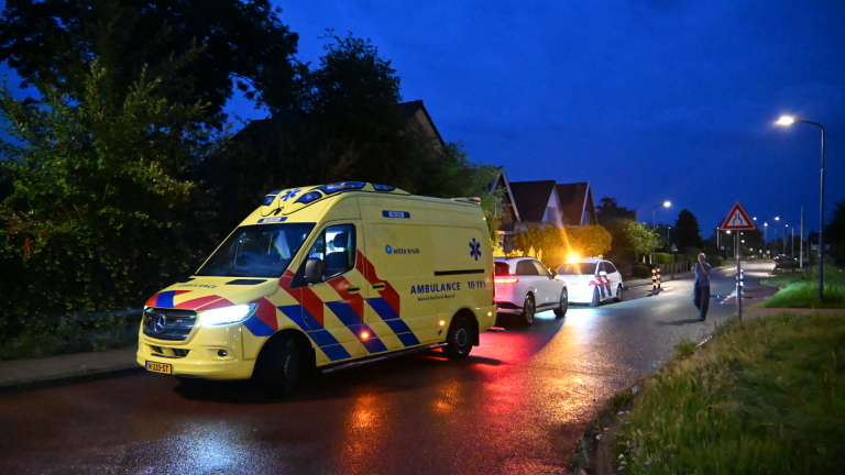Een politieauto en een ambulance staan 's nachts op een donkere weg geparkeerd.