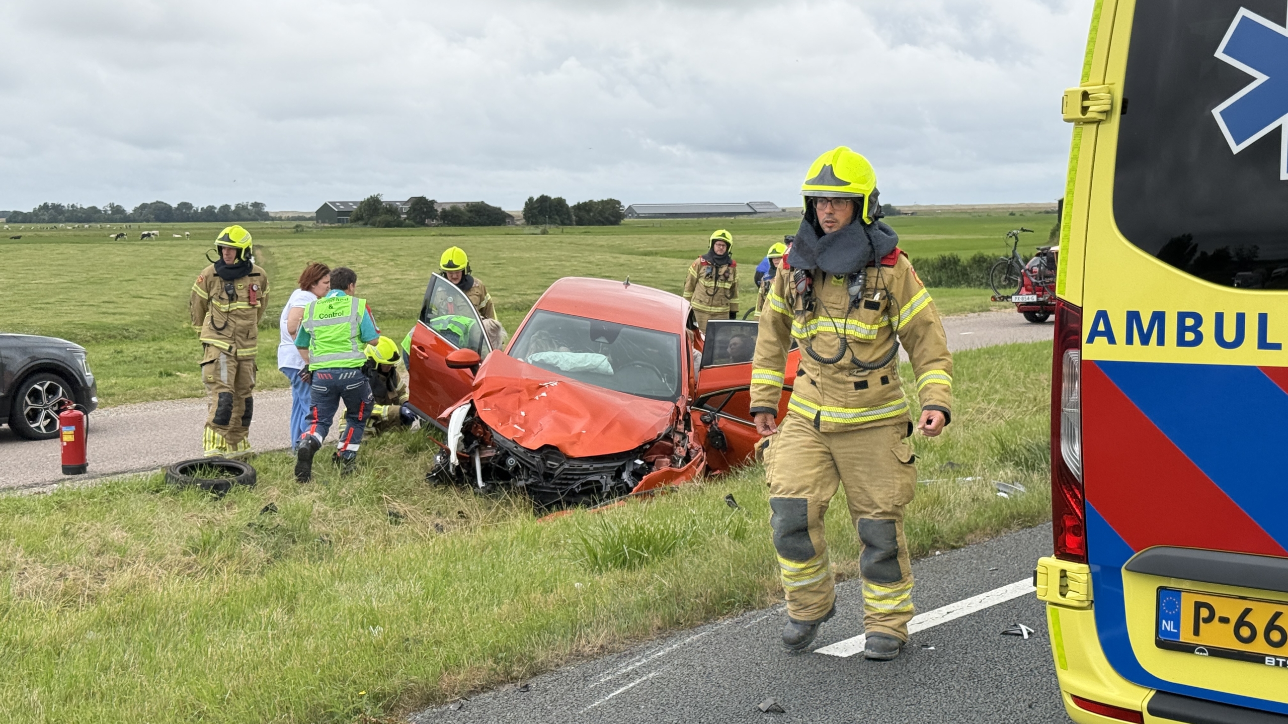 Verkeersongeval op een snelweg met betrokken auto's, brandweerlieden en twee ambulances aanwezig, omstanders kijken toe.