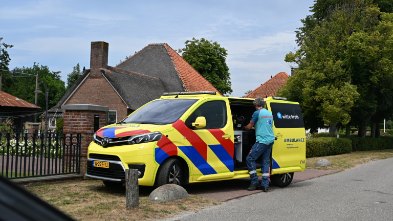 Gele ambulancebus van Witte Kruis met open schuifdeur, terwijl een hulpverlener spullen pakt naast een huis
