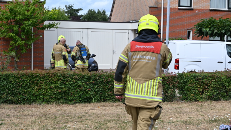Brandweerlieden in beschermende kleding bij een woning met garage, één loopt naar de groep bij een auto