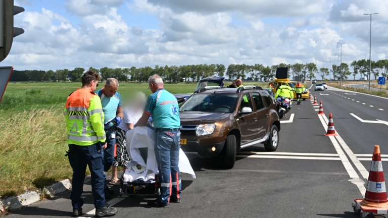 Hulpverleners verzorgen een slachtoffer naast een auto op een afgezet wegvak met pionnen en hulpdiensten op de achtergrond