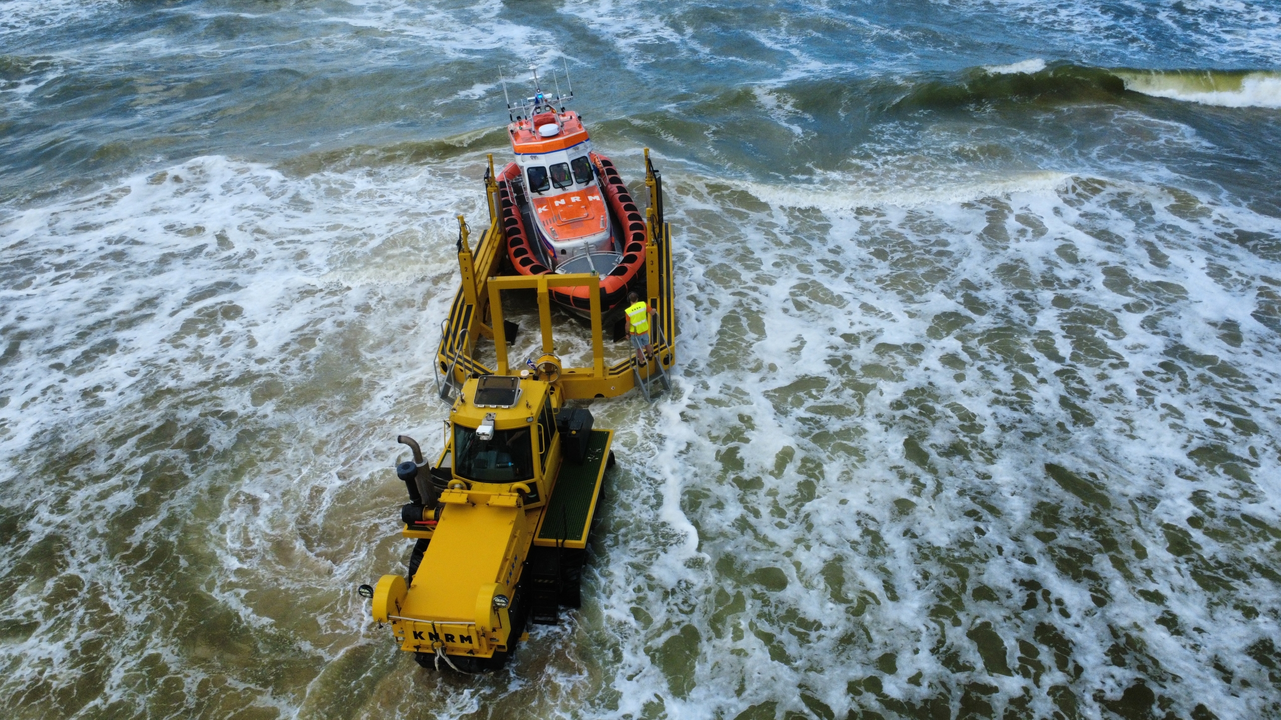Reddingsbrigade in oranje rubberboot vaart over ruwe zee, met windturbines op de horizon