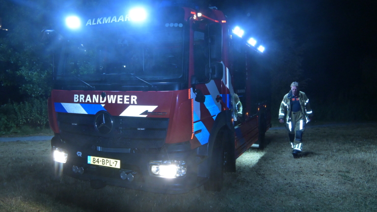 Politie en brandweer onderzoeken ’s nachts een rokende motorfiets die op zijn kant ligt in het gras