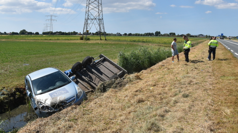 Beschadigde auto in een sloot naast een omgekantelde aanhanger in een landelijk gebied