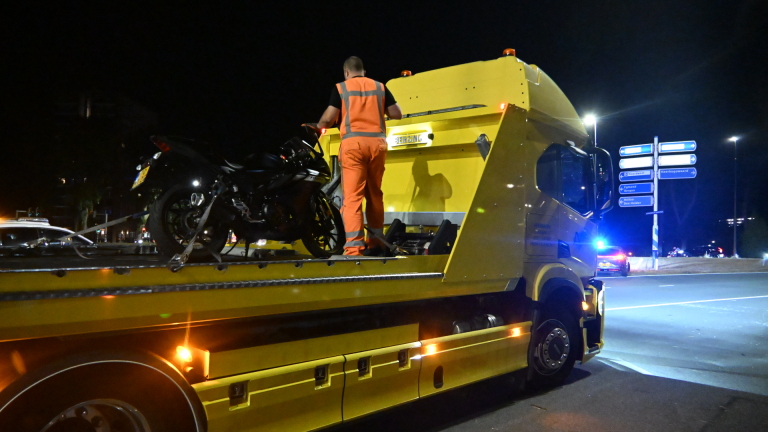Politieauto en ambulance met zwaailichten bij nachtelijk ongeval; motorfiets en helm op de weg, agent regelt verkeer