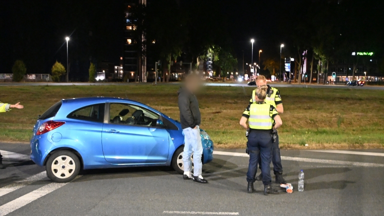 Politieagent in reflecterend vest regelt ’s avonds verkeer op rotonde, met auto’s en blauwe zwaailichten op de achtergrond