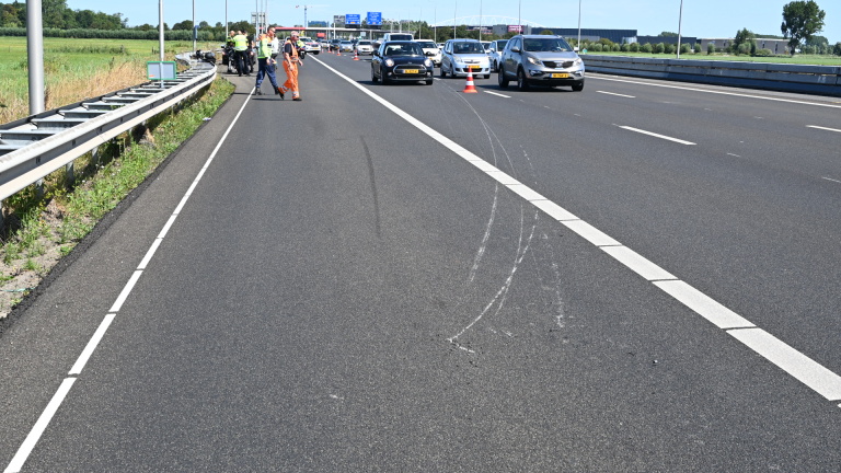 Politieagenten en motor op de snelweg bij een met pionnen afgezet incident, met politieauto en file op de achtergrond