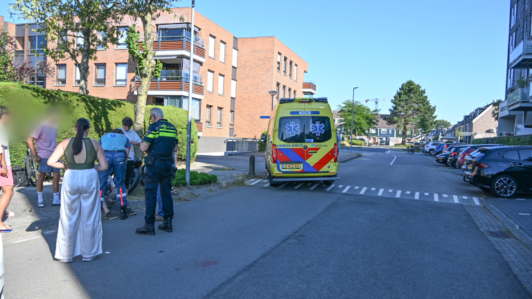 Politieagent op fiets bij gele ambulance met open achterdeuren, terwijl een ambulancebroeder helpt op straat