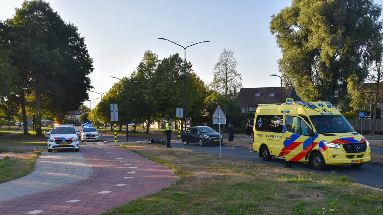 Voorruit van een auto met grote barst en spinwebscheuren na een aanrijding, met politieauto op de achtergrond