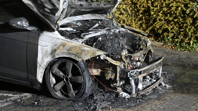 Brandweerman blust brandende auto met zwaar beschadigde voorkant, met open motorkap en rook in het donker